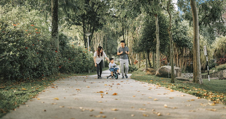 A couple walks down a path with their young son on a bike
