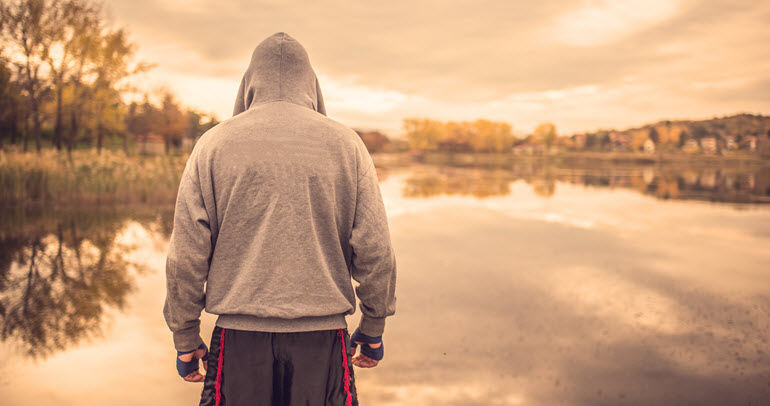 A man, dressed in boxing gear, looks out over a lake