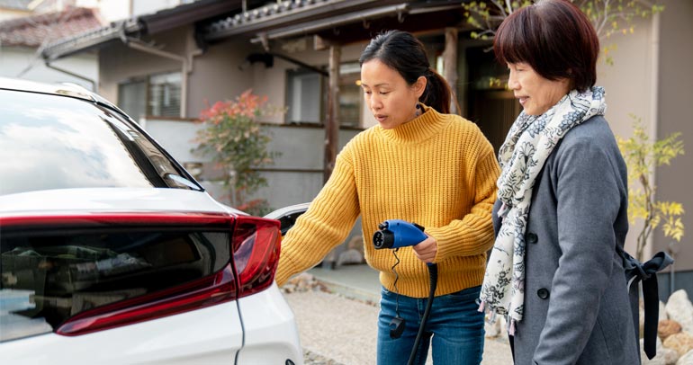 A woman is showing her friend how to connect the plug and charge her battery electric vehicle.