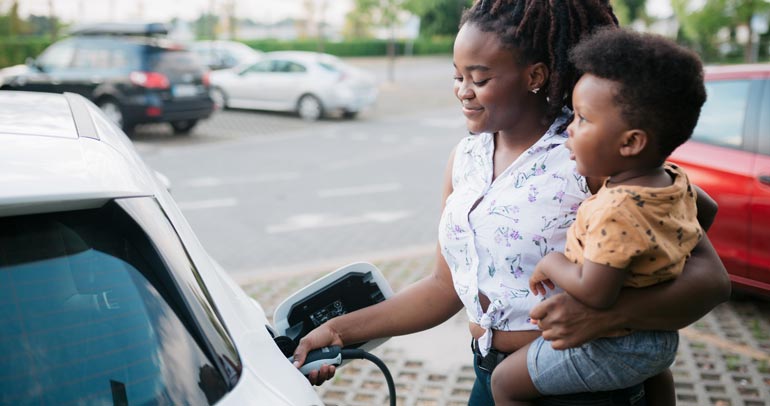 A woman charging her EV while holding her child.