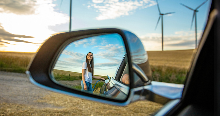 A woman standing outside her electric vehicle near a windmill farm