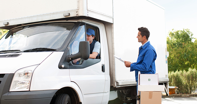 A man receiving a delivery of boxes is standing next to the delivery person who is sitting inside a white box van