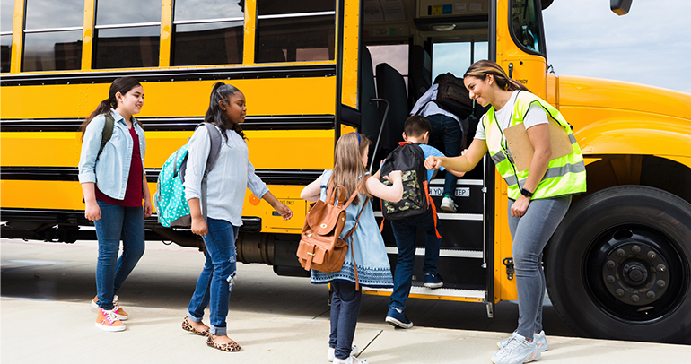 Kids getting on a school bus with the help of their bus driver