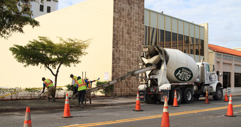 A work crew laying down concrete on the sidewalk from a class 8 commercial concrete truck