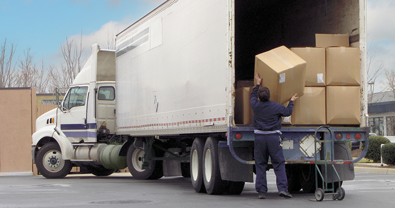 A Class 8 commercial vehicle driver unloads their tractor trailer truck to make a delivery