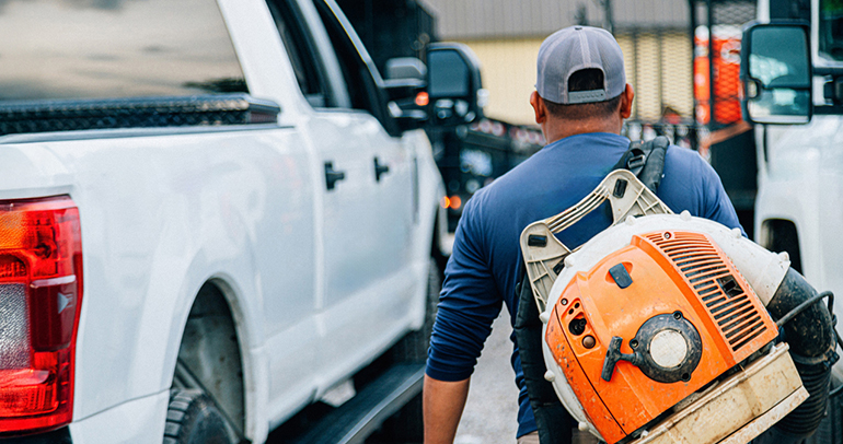 A man carrying a leaf blower from the job sit to his pickup truck