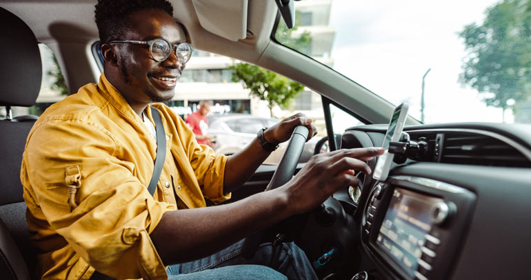 A young male driver is interacting with his smartphone in his electric vehicle (EV)