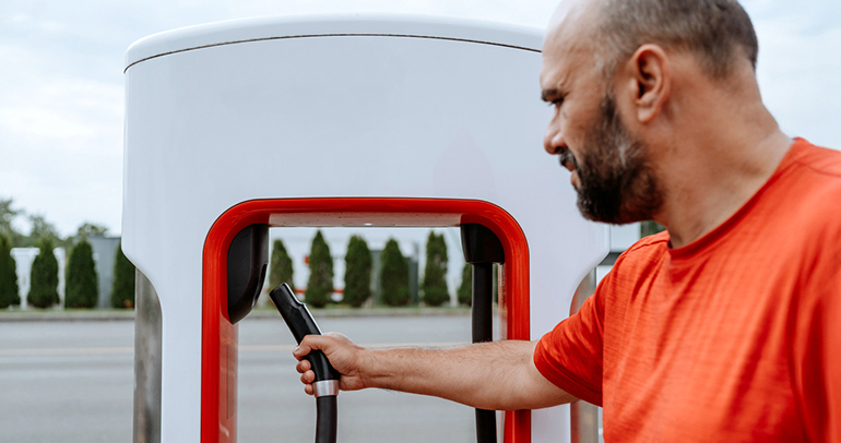 A man using a Tesla public charger to charge his battery electric vehicle (BEV)