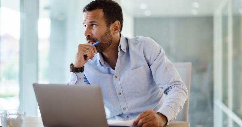 A fleet business decision-maker is at his desk, looking pensively away from his laptop as he's thinking about his business operations and possible fleet technology investments