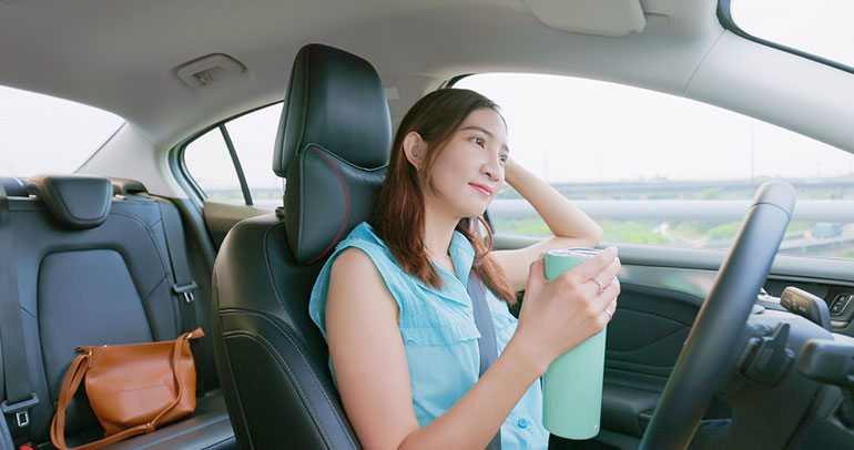 A woman sitting in the driver’s seat of an autonomous car, holding a travel mug and looking out the window