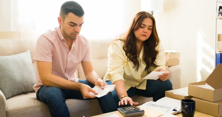 A couple reviews bills and calculates expenses from their Texas retail electric provider at a table in their living room